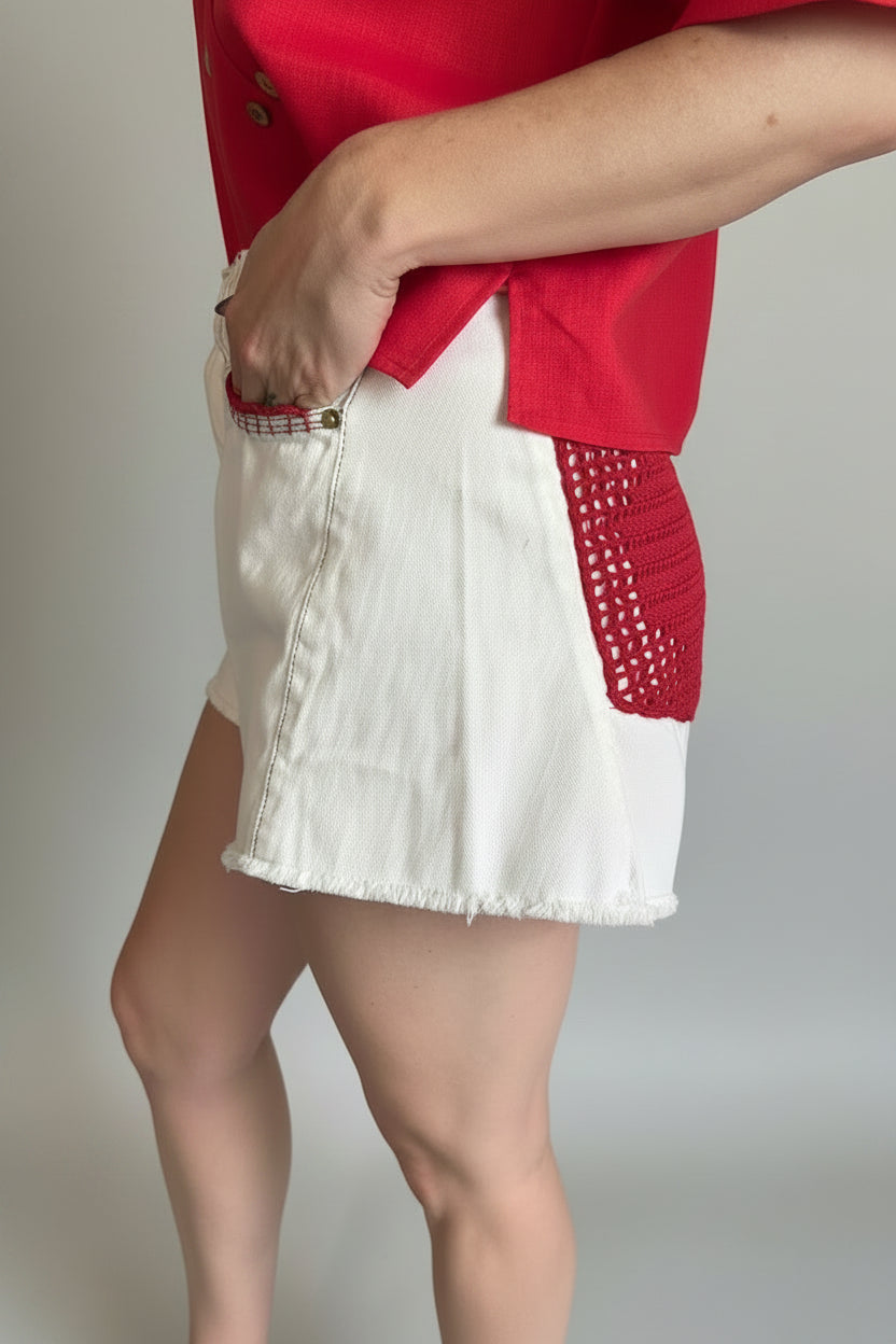 person wearing a white jean short with red crochet lace on back pocket and on the trim of the front pocket